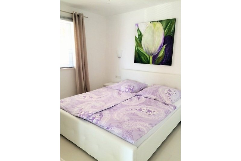 Schlafzimmer mit lila Bettwäsche und Holzmöbeln.