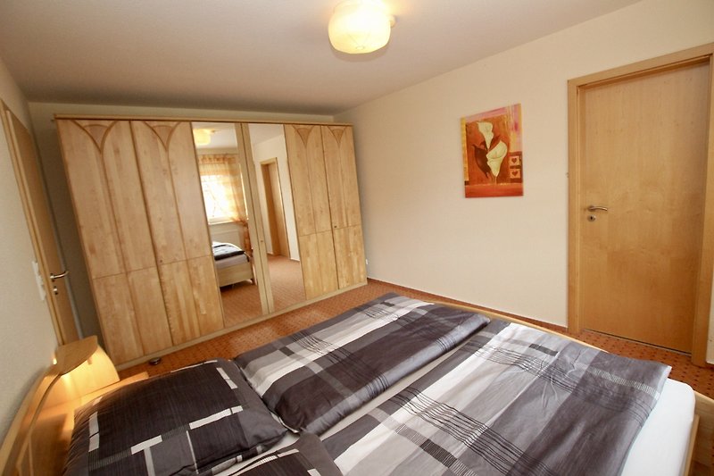 Das 1. Schlafzimmer mit Holzbett, Vorhängen und gemütlicher Beleuchtung.