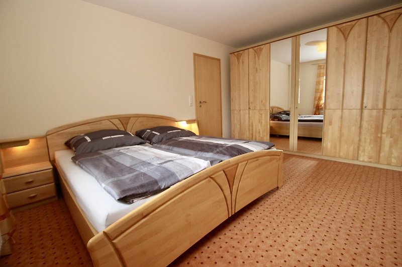 Das 1. Schlafzimmer mit Holzbett, stilvoller Beleuchtung und Vorhängen.