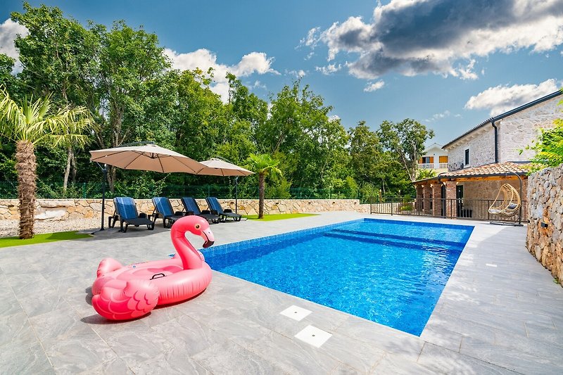 Luxuriöser Poolbereich mit Palmen, Liegestühlen und Sonnenschirmen.