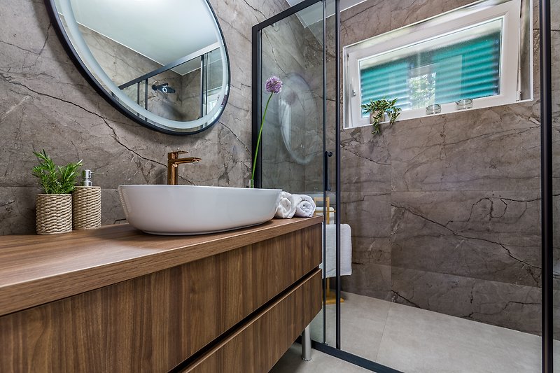 Modernes Badezimmer mit Spiegel, Armatur, Pflanze und Fenster.