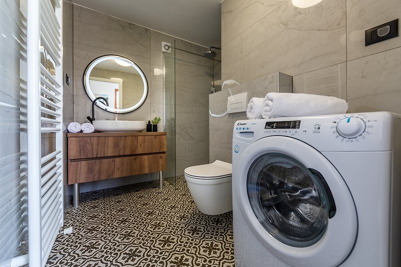 Modernes Badezimmer mit Waschmaschine, Trockner, Spiegel und Schrank.