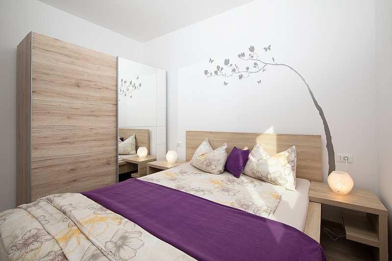 Gemütliches Schlafzimmer mit lila Bett und Holzmöbeln.