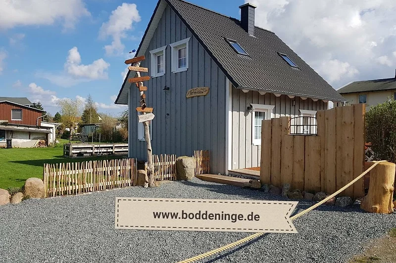 Holzhaus mit Veranda und Garten, umgeben von einem Lattenzaun.