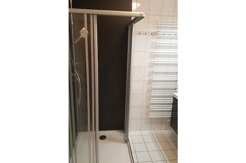 Moderne Badezimmerausstattung mit Glasduschtür, Fliesenboden und Regal.
