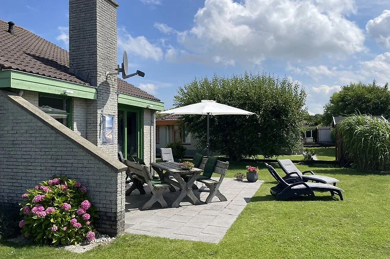 Großer Garten mit Sitzbereich, gepflegtem Rasen und schattiger Terrasse.