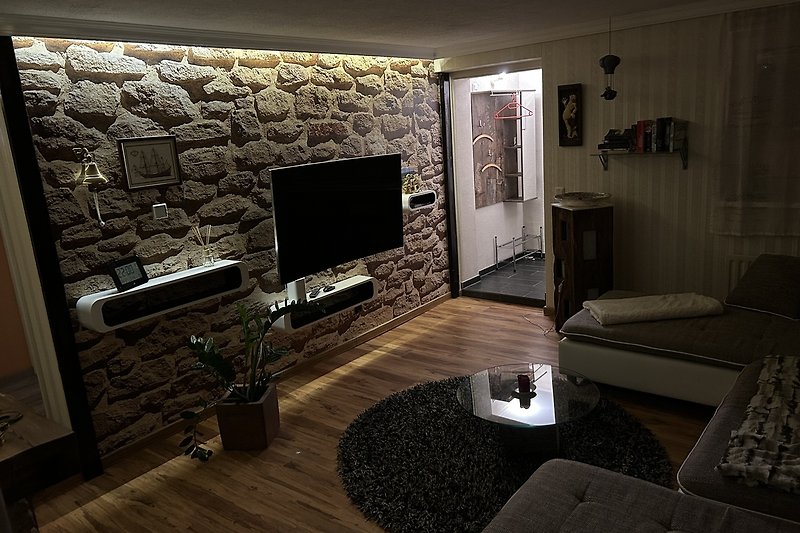 Gemütliches Wohnzimmer mit Holzboden, Couch und Fernseher.