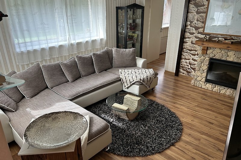 Wohnzimmer mit großer Couch, Tisch, Bilderrahmen und Vorhängen.