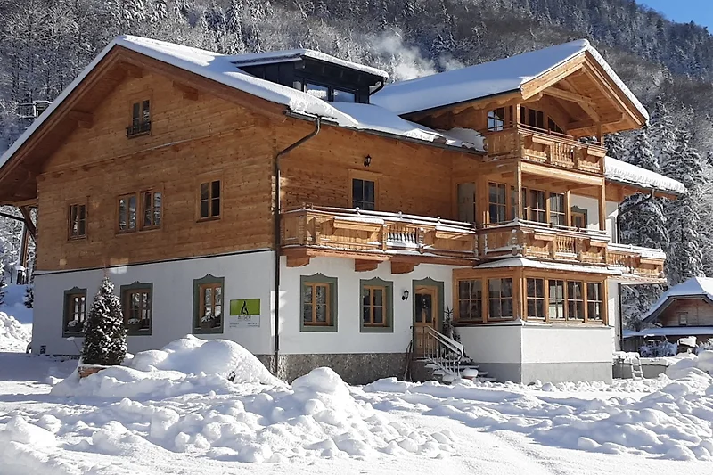 Verschneites Dorf mit Berghütte und Gasthof in frostiger Winterlandschaft.