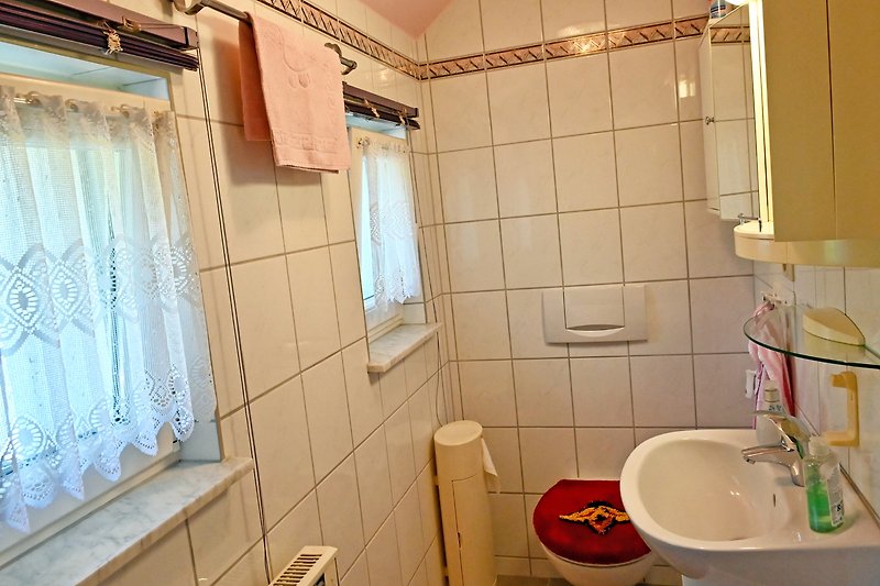 Gemütliches Badezimmer mit lila Vorhang, Spiegel und Holzfenster.