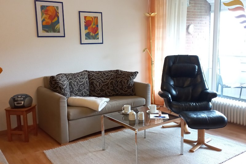 Wohnzimmer mit Couch, Couchtisch und großen Fenstern.