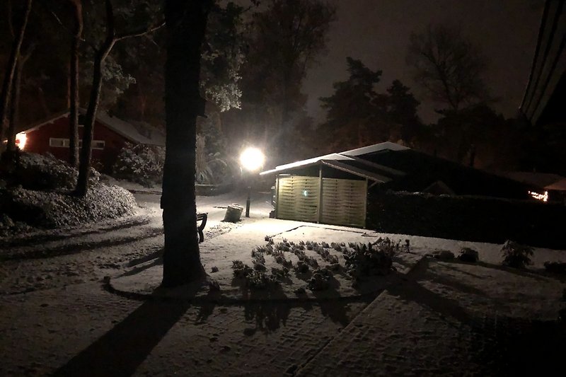 Gemütliches Cottage in winterlicher Landschaft mit Schnee und Straßenbeleuchtung.