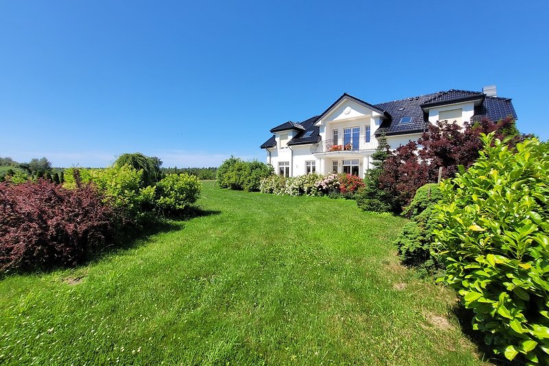 Schönes Haus mit grünem Garten, blauem Himmel und natürlicher Landschaft.