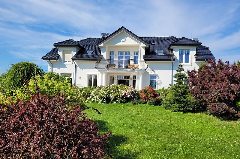 Schönes Haus mit blühenden Pflanzen, grünem Rasen und blauem Himmel.
