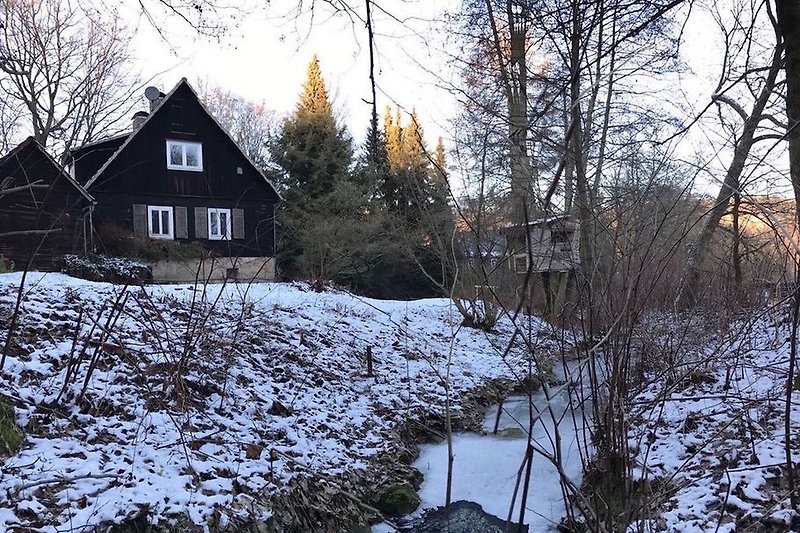 Winterliche Außenansicht auf das Haus und den zugefrorenen Bach