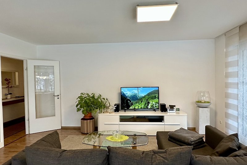 Gemütliches Wohnzimmer mit Couch, Fernseher und Pflanzen.