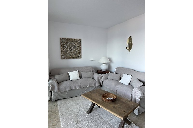 Wohnzimmer mit grauem Sofa, Holztisch und Kunst.