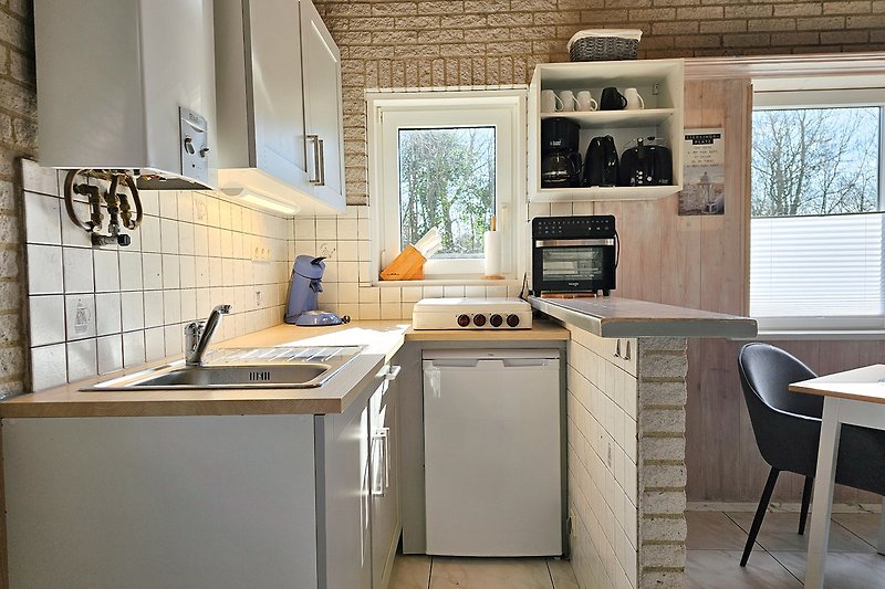 Moderne Küche mit Holzmöbeln, Fenster, Küchengeräten und Esstisch.