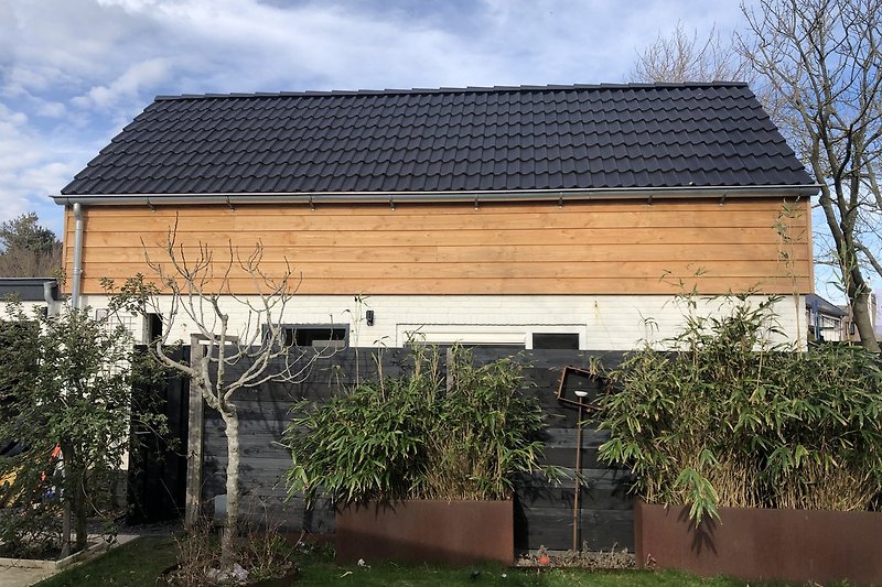 Fassade mit Holzverkleidung, Hausdach und Garten.
