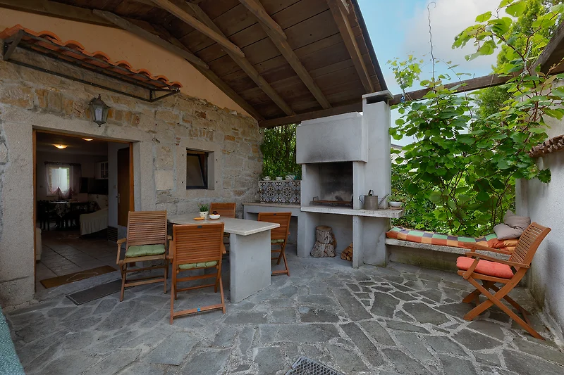 Landhaus mit Steintisch, Gartenstühlen, Pflanzen und schattigem Sitzplatz.
