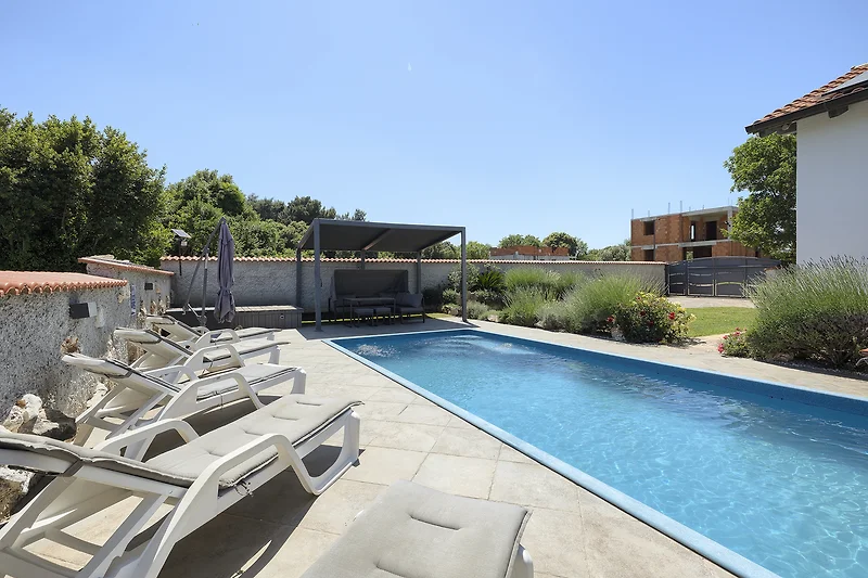 Poolbereich mit Liegestühlen vor einer Villa in der Wohnanlage.
