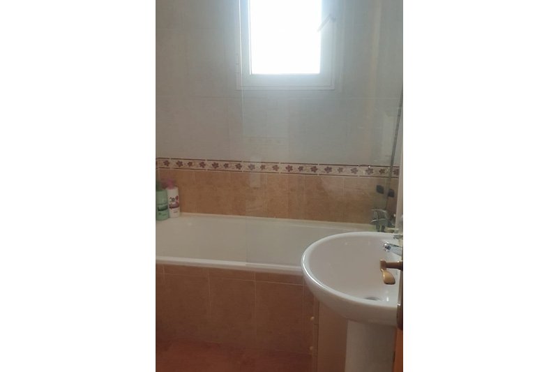 Badezimmer mit Badewanne, Waschbecken, WC, Heizung Spiegel und Fliesen.