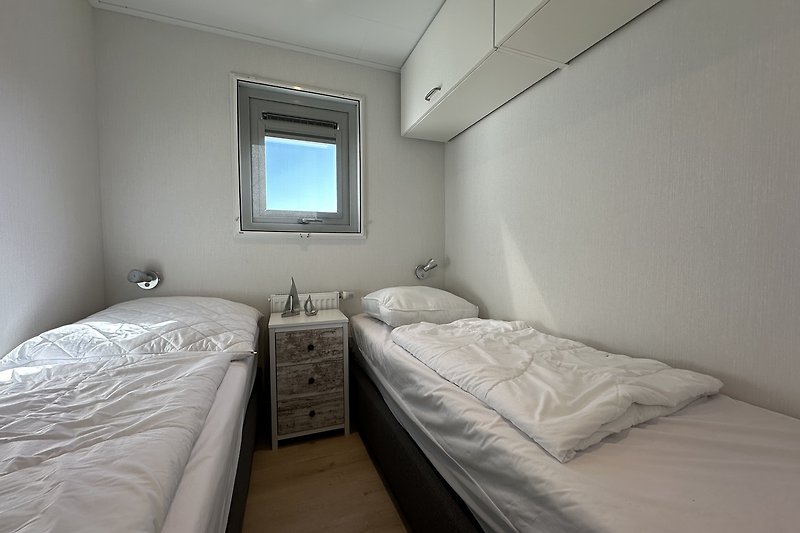 Schlafzimmer mit grauem Bett, Fenster und Fernseher.