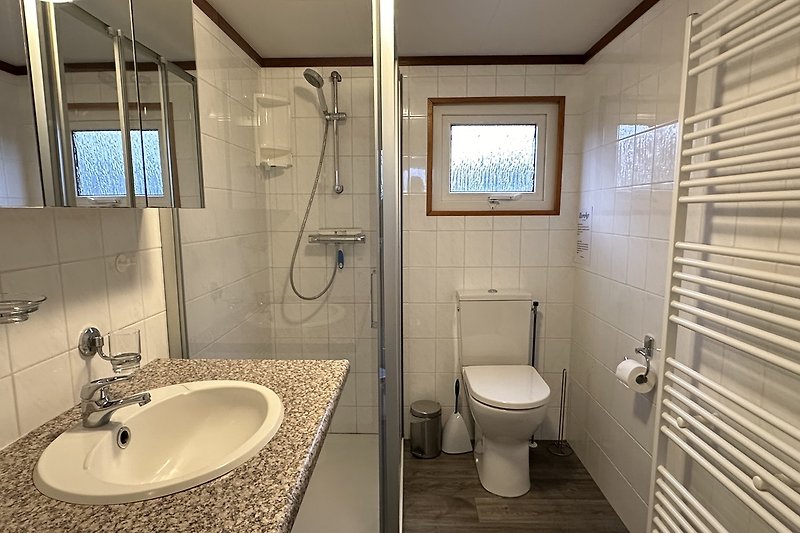 Badezimmer mit lila Wand, Dusche, Spiegel & Fenster.