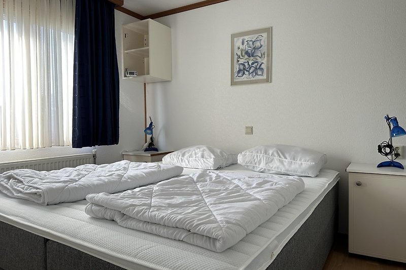 Elegantes Schlafzimmer mit grauem Bett, Holzmöbeln und Vorhängen.