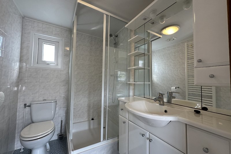 Modernes Badezimmer mit lila Armaturen, Glasdusche und Fenster.
