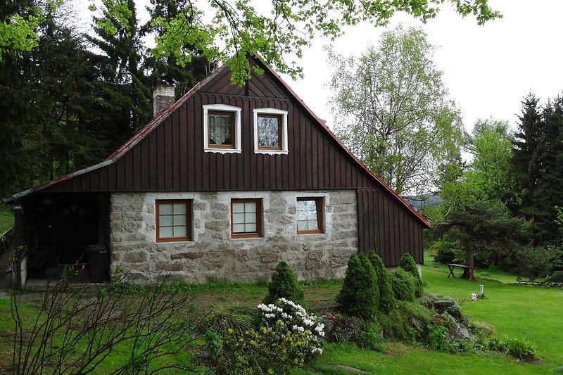 Gemütliches Holzhaus mit Garten, Blumen und Wald im Hintergrund.