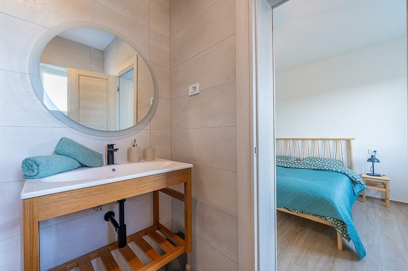 Badezimmer mit Spiegel, Waschbecken, Armaturen und Holzakzenten.