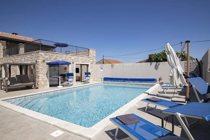 Poolterrasse mit Liegen und schattigem Sitzbereich.