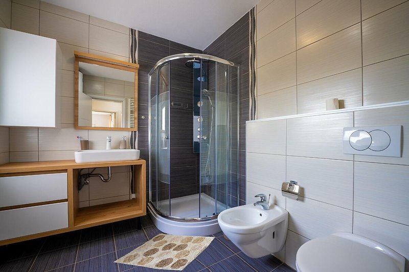 Entspannen Sie in diesem modernen Badezimmer mit stilvoller Einrichtung und hochwertigen Armaturen. Genießen Sie eine erfrischende Dusche oder ein entspannendes Bad.