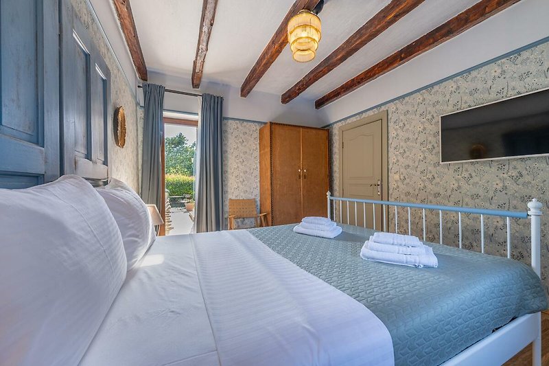 Komfortables Schlafzimmer mit Holzbett, Fenster mit Vorhängen und gemütlicher Bettwäsche.