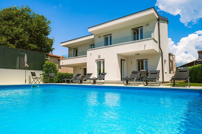 Luxuriöses Haus mit Pool, umgeben von Natur und blauem Himmel.