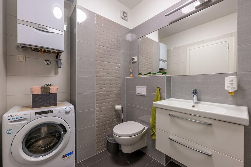 Badezimmer mit lila Akzenten, Waschmaschine, Trockner und Spiegel.