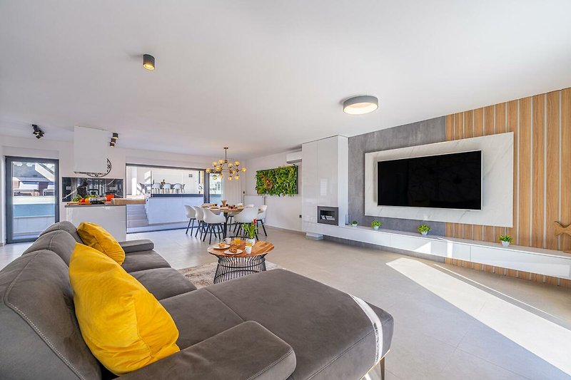 Modernes Wohnzimmer mit bequemer Couch, Fernseher, Holztisch und Pflanzen. Gemütliche Atmosphäre.