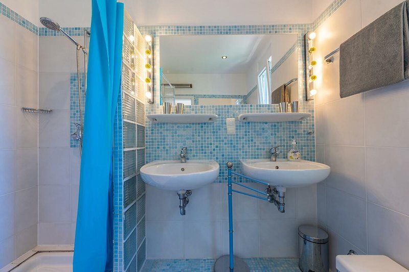 Badezimmer mit Spiegel, Wasserhahn, Waschbecken und Fliesen.