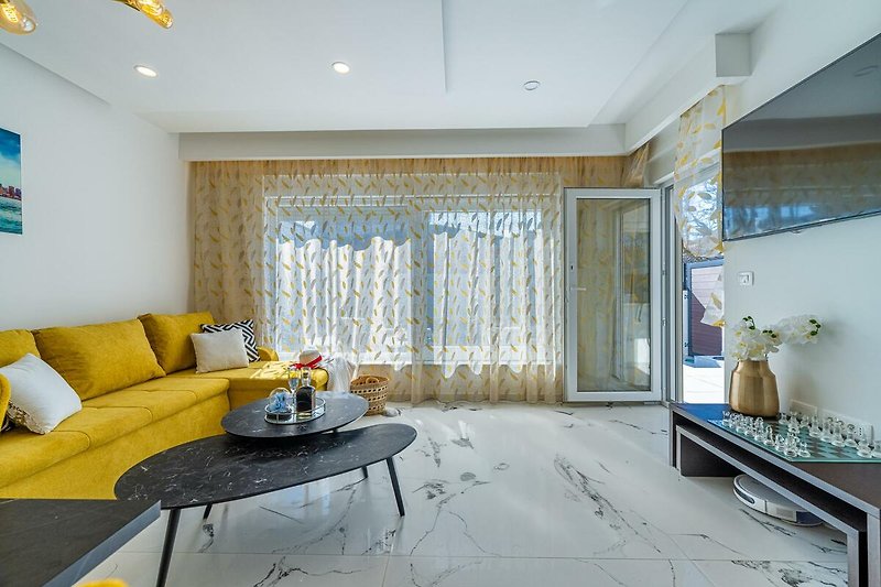 Wohnzimmer mit gelber Couch, Holzmöbeln und Vorhängen.