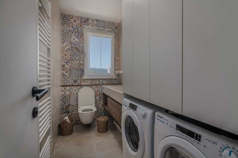 Moderne Waschküche mit Spiegel und Waschmaschine. Hier können Sie Ihre Wäsche bequem waschen und trocknen.