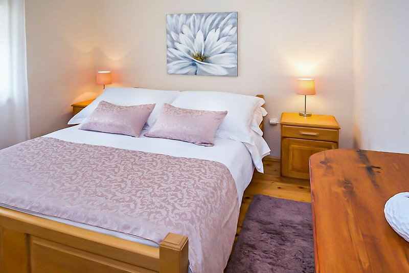 Udobna spavaća soba s drvenim namještajem i svijetlim tekstilom.