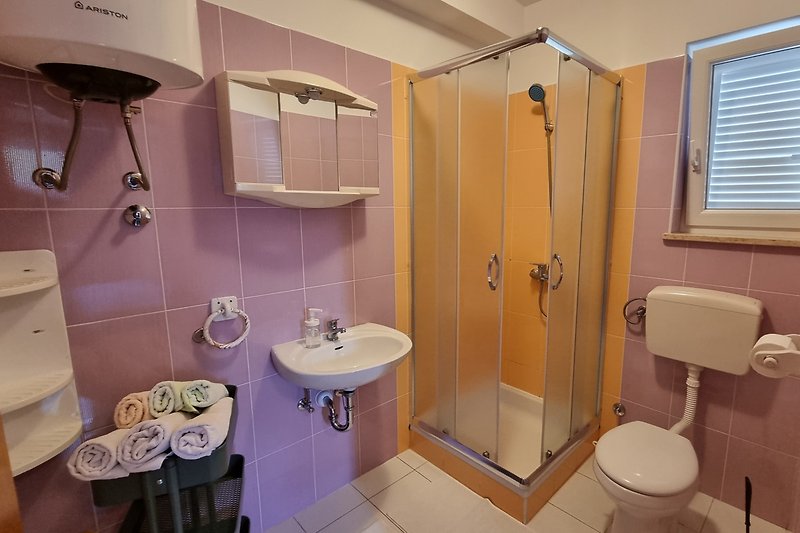 Badezimmer mit lila Akzenten, Spiegel, Toilette, Dusche und Fenster.