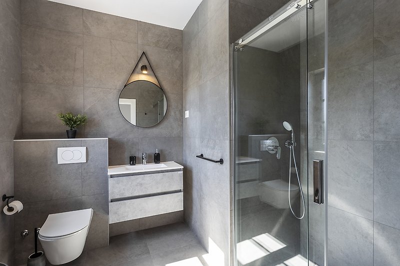 Moderan dizajn kupaonice s ogledalom, umivaonikom i tušem.