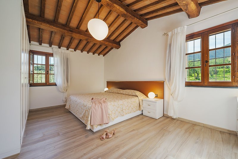 Schlafzimmer mit Bett, Fenster, Holzbalken und gemütlicher Einrichtung.