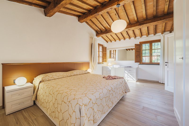 Schlafzimmer mit gemütlichem Bett, Holzbalken und Lampenschirm.