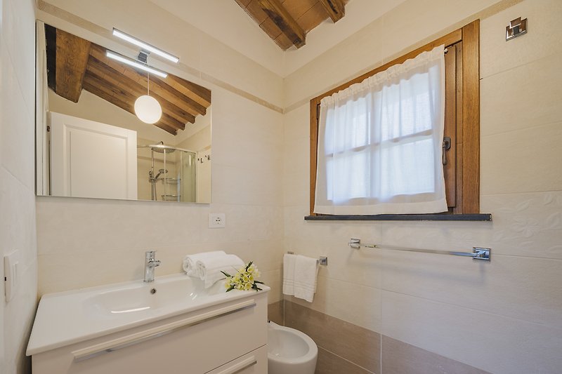 Bad mit Fenster, Badewanne, Spiegel und Holzmöbeln.