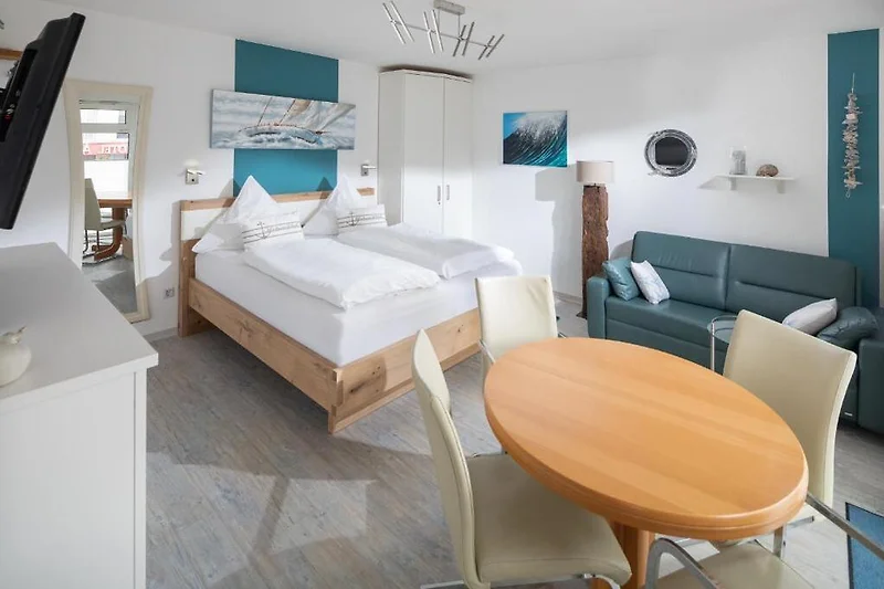 Schlafzimmer mit Doppelbett, Sessel, Esstisch und grüner Zimmerpflanze.