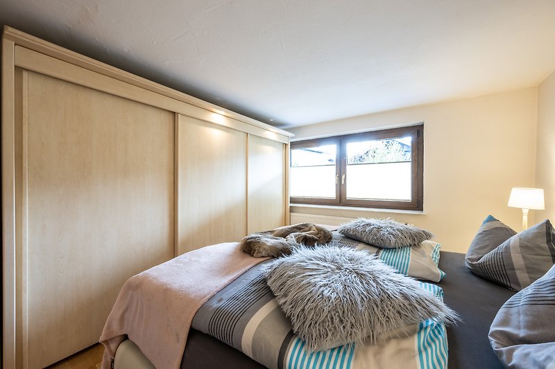 Gemütliches Schlafzimmer mit Holzbett, Fenster und gemütlicher Beleuchtung.