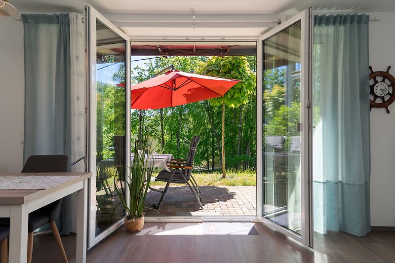 Gemütliche Terrasse mit Holztisch, 4 Stühlen Sonnenschirm und Pflanzen.